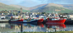 Fishing trawlers docked in Dingle Harbour with pastel houses and mountains in the background on the Dingle Peninsula, County Kerry.