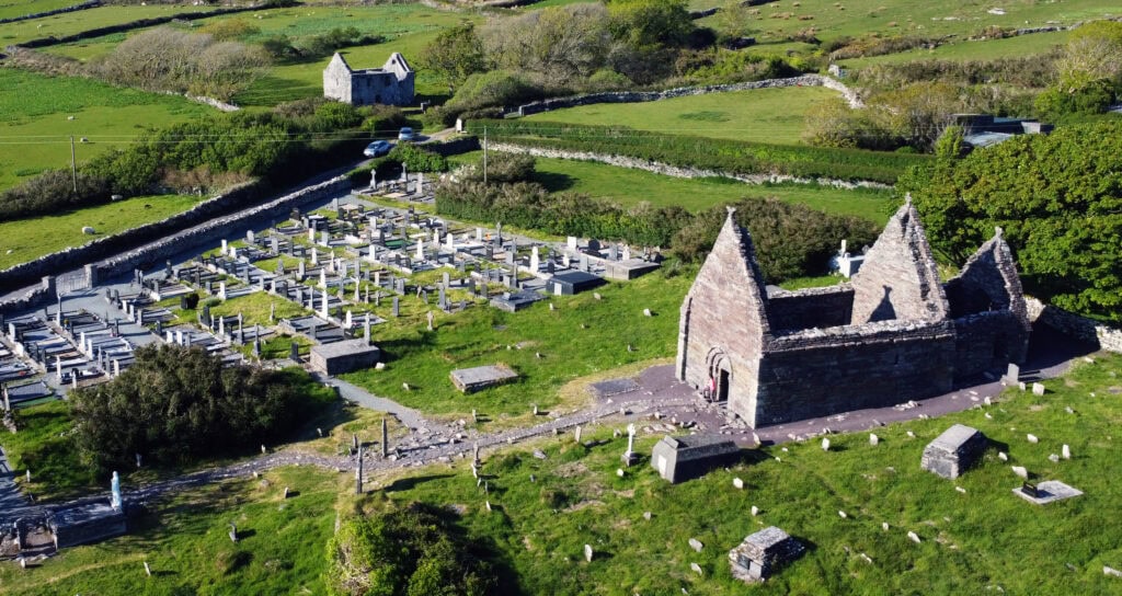 Aerial image of the ruins of Kilmalkedar Church with graveyard and surrounding landscape.