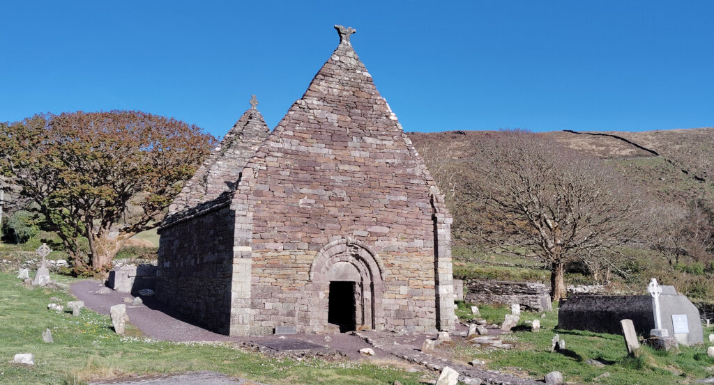 Image of the stone ruins of Kilmalkedar Church with Celtic and Christian carvings in the foreground.