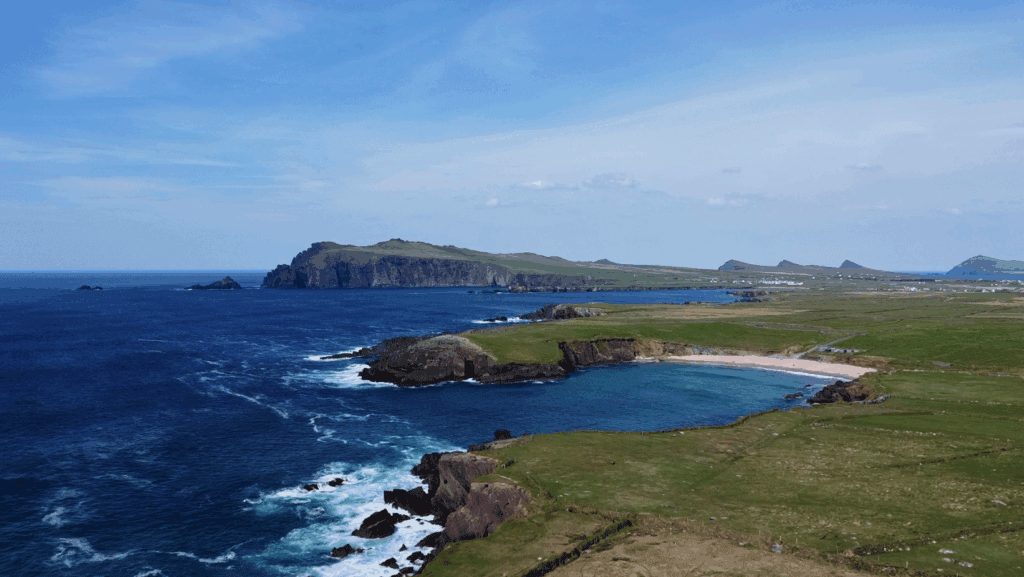 Slea Head coastline with cliffs, blue Atlantic waves and a small sandy cove on the Dingle Peninsula.