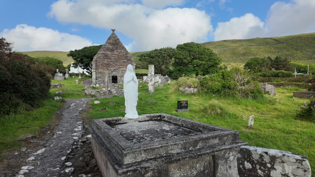 Statue within the graveyard at Kilmalkedar Church with the medieval church and historic stone crosses in the background, County Kerry.