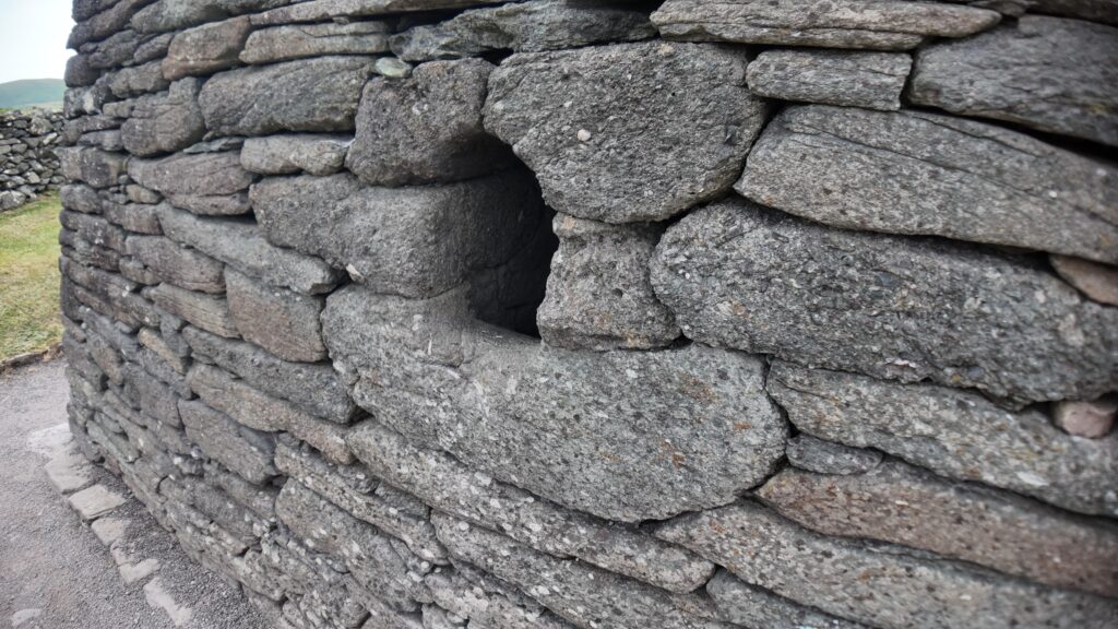 Small east-facing window set within the thick dry-stone wall of Gallarus Oratory, illustrating its carefully crafted sandstone masonry.