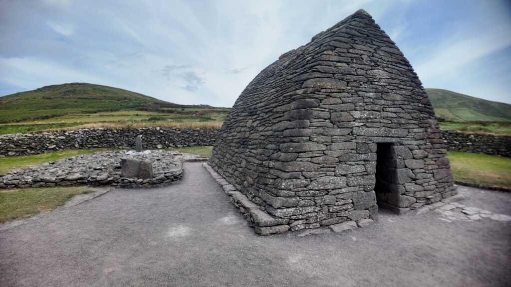 Side view of Gallarus Oratory showing its original west doorway, corbelled stone roof and surrounding stone enclosure on the Dingle Peninsula.