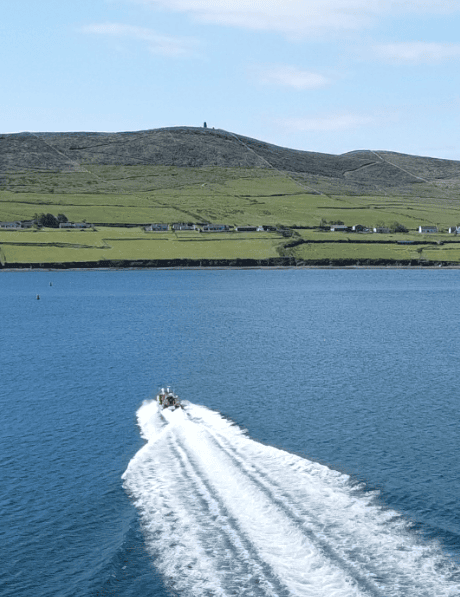 A motorboat crosses Dingle Harbour with Eask Tower visible on Carhoo Hill in the background, County Kerry.