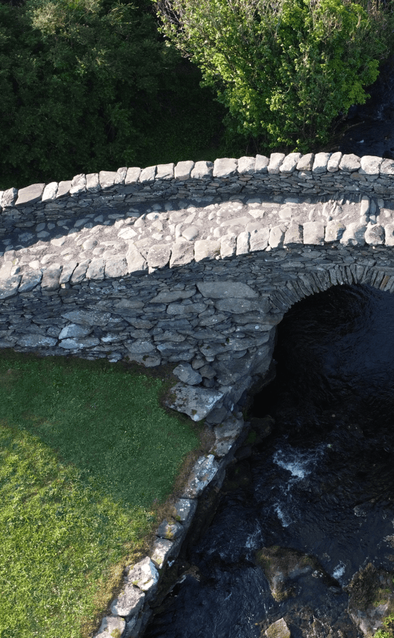 Oblique aerial view of Garfinny Bridge showing its stone arch, parapet walls and traditional stone-paved deck above the Garfinny River.