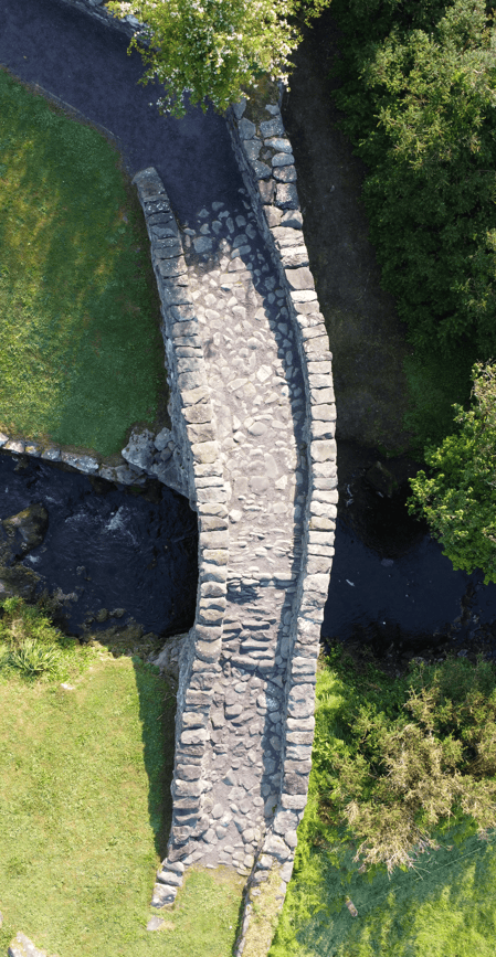 Overhead view of Garfinny Bridge showing its stone-paved deck and curved parapet walls crossing the Garfinny River near Dingle.