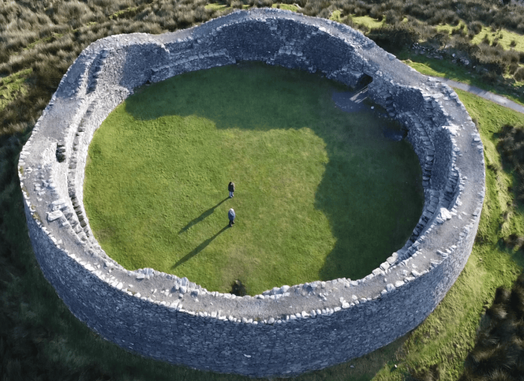 Aerial view inside Staigue Fort showing its circular grass-covered enclosure, thick dry-stone walls and narrow entrance passage.