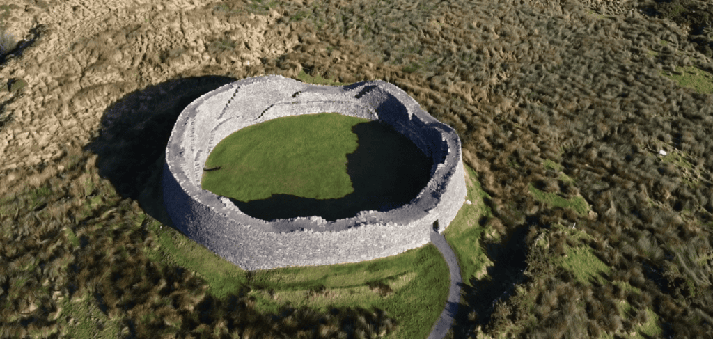 Aerial view of Staigue Fort showing its near-circular dry-stone enclosure, grass-covered interior and surrounding landscape.