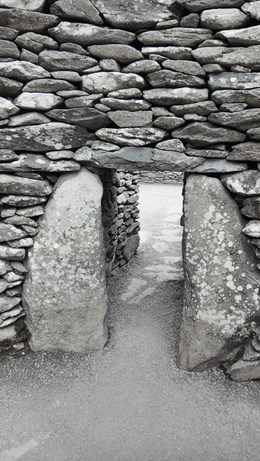 Narrow entrance through a Fahan dry-stone wall framed by two large upright stone slabs leading into the enclosed site.