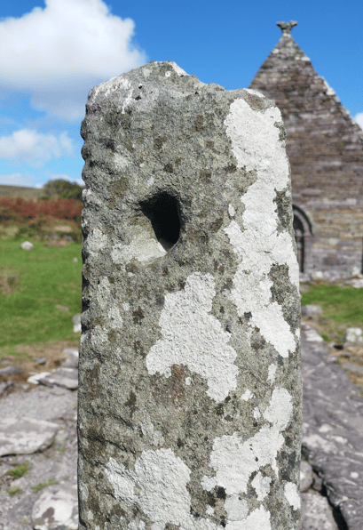 Close view of the Kilmalkedar Ogham Stone showing the circular hole through its weathered upper section beside Kilmalkedar Church.