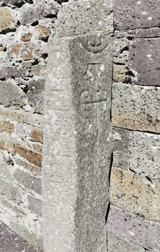 Close view of the Kilmalkedar Ogham Stone showing carved markings on its weathered surface beside the church wall.