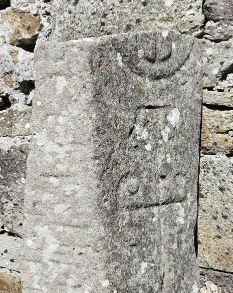 Carved cross and weathered symbols on the face of the Kilmalkedar Ogham Stone beside the historic church masonry.