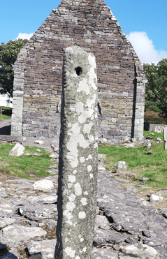 Kilmalkedar Ogham Stone standing upright in the graveyard with the gable wall of Kilmalkedar Church directly behind it.