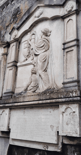 Carved stone memorial with draped figures, architectural panels and a weathered inscription at Muckross Abbey.