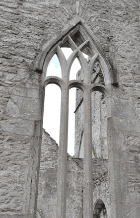 Tall pointed Gothic window with stone tracery surviving within the ruins of Muckross Abbey in Killarney National Park.