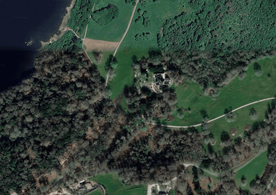 Aerial view of Muckross Abbey surrounded by woodland and open fields beside the lakeshore in Killarney National Park.