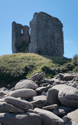 Minard Castle ruins standing above the large rounded boulders of Kilmurry Bay on the southern Dingle Peninsula.