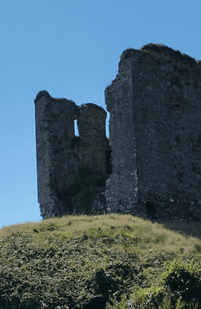 Ruined stone walls of Minard Castle with exposed interior sections rising above a grassy slope on the Dingle Peninsula.