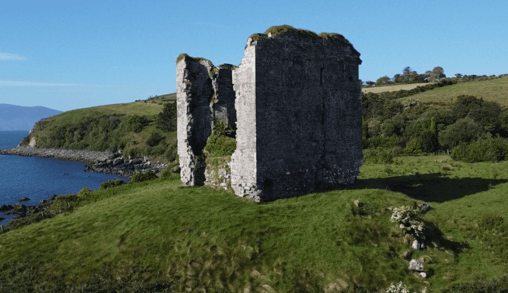Ruined stone walls of Minard Castle overlooking the rocky shoreline and Kilmurry Bay on the Dingle Peninsula.