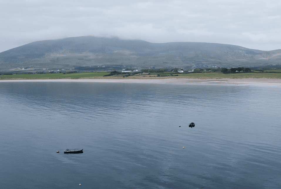 Ventry Beach stretching beneath mist-covered hills with small boats floating on the calm waters of Ventry Harbour.