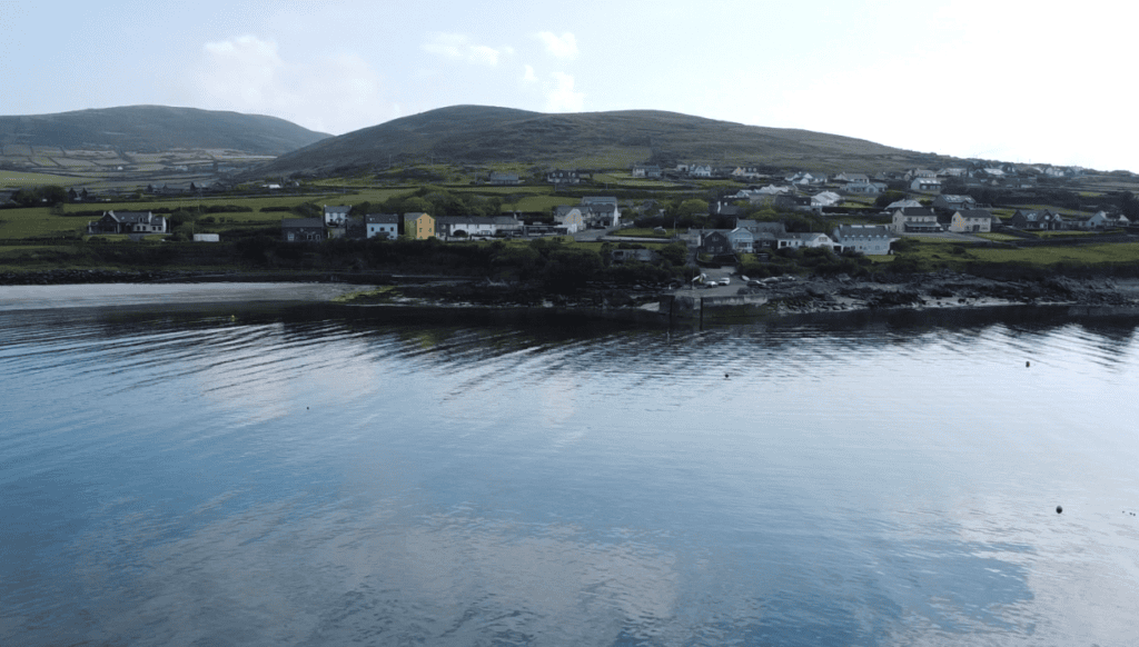 Ventry village and surrounding green hills reflected in the calm waters of Ventry Harbour on the Dingle Peninsula.