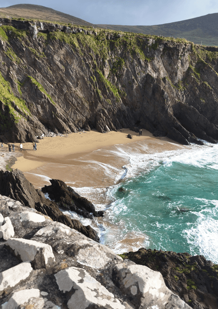Coumeenoole Beach beneath steep rocky cliffs, with Atlantic waves washing across the sandy cove on the Dingle Peninsula.