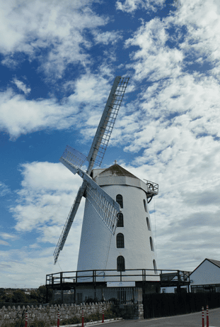 Blennerville Windmill with its four sails extending against a blue and cloud-filled sky near Tralee in County Kerry.