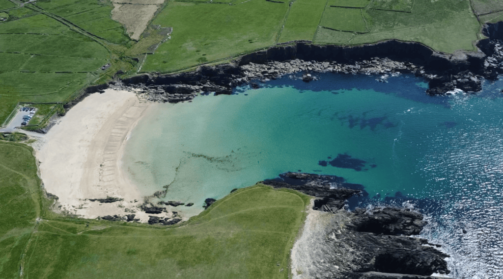 Aerial view of Clogher Strand showing the curved sandy beach, turquoise Atlantic water, rocky shoreline and surrounding green fields.