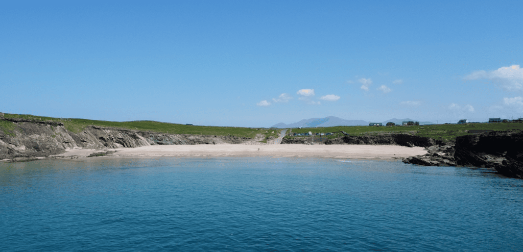 Aerial view of Clogher Strand showing the sandy Atlantic beach, rocky headlands, green fields and mountains of the Dingle Peninsula.