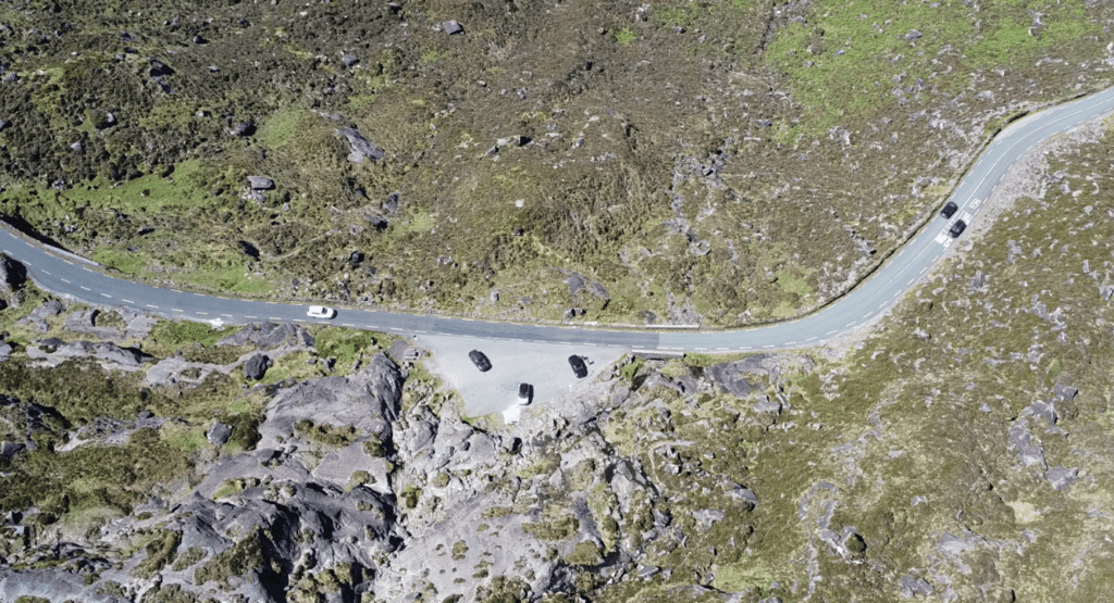 Aerial view of the Conor Pass summit road curving between rocky mountain slopes with several vehicles parked beside the road.