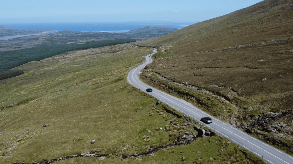 Winding Conor Pass road crossing the mountain slopes of the Dingle Peninsula with cars travelling through the open landscape.