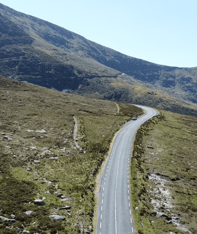 Conor Pass road climbing through steep rocky mountain slopes on the Dingle Peninsula with a car travelling towards the pass.