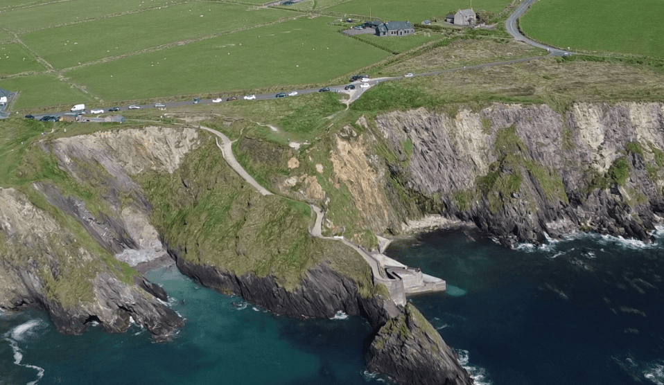 Aerial view of Dunquin Pier beneath steep sea cliffs, with the winding access path descending from the surrounding farmland.