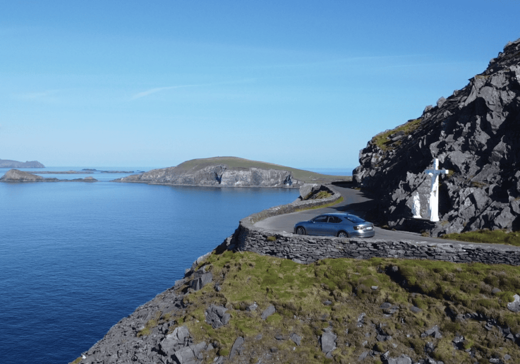 Slea Head Drive curving around a rocky coastal headland with Atlantic waters and offshore islands beyond.