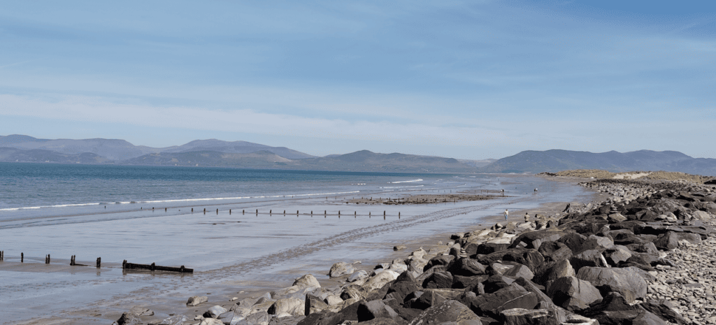 Rossbeigh Strand stretching along Dingle Bay, with a broad sandy shoreline, coastal dunes and mountains across the water.