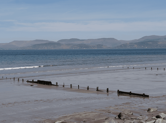 Wide sandy foreshore at Rossbeigh Strand with old timber structures exposed at low tide and mountains across Dingle Bay.