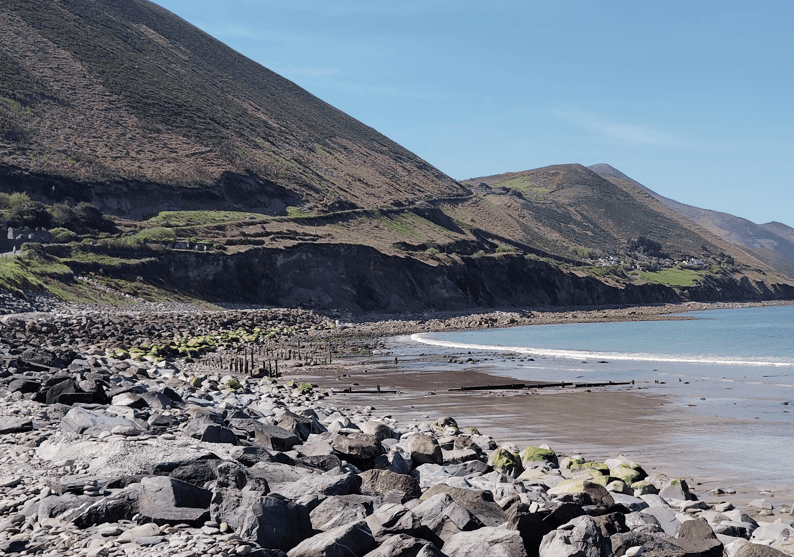 Rocky shoreline and sheltered bay at Rossbeigh Strand, with steep coastal slopes rising beside the beach in County Kerry.
