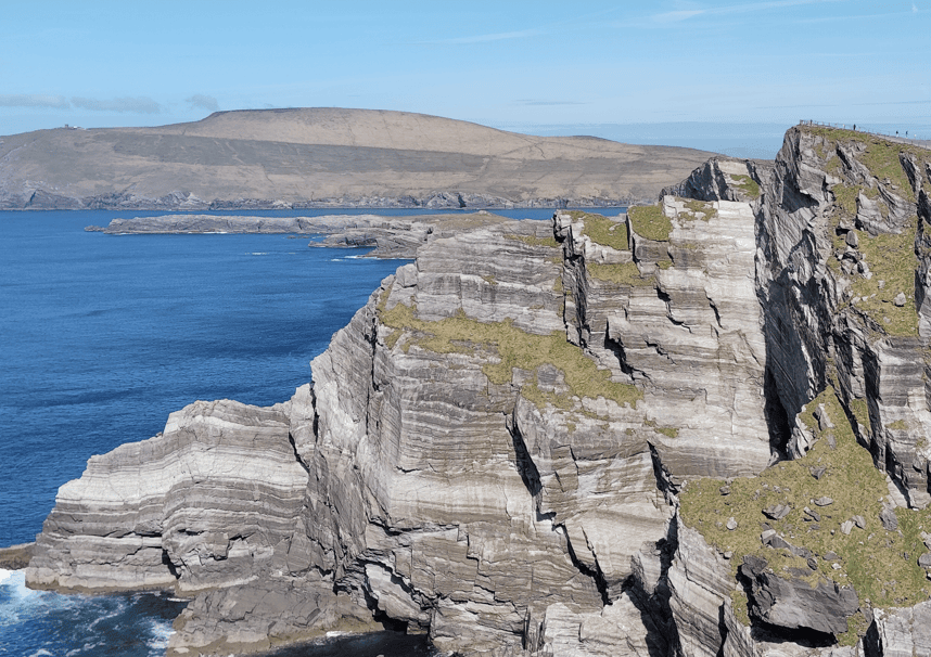 Layered rock faces and grass-covered tops of the Kerry Cliffs extending along the Atlantic coastline in County Kerry.