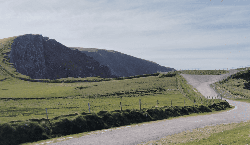 Access road and parking area at the Kerry Cliffs visitor site, surrounded by open grassland near the Atlantic coast.