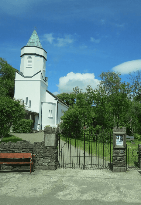 St Michael’s Catholic Church in Sneem, with its distinctive tower and spire rising above trees beside the village street.