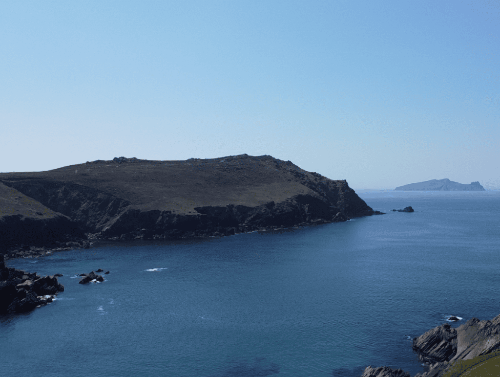 Rocky cliffs and dark slopes of Clogher Head extending into blue Atlantic waters beneath a clear sky.