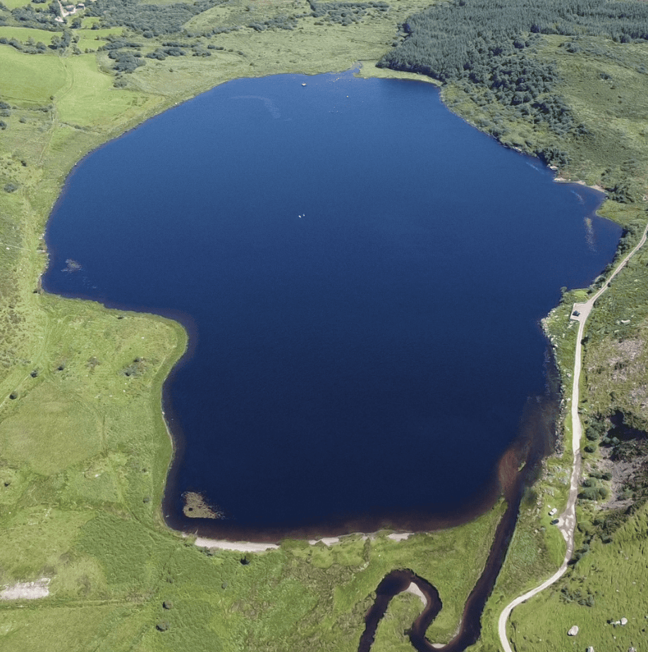 Annascaul Lake surrounded by rocky mountain slopes and rough upland pasture.